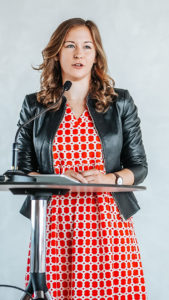 Claudia Bauer spricht an einem Mikrofonständer bei einer Indoor-Veranstaltung.