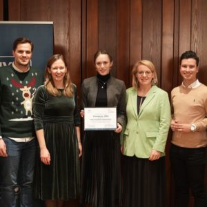 Gruppe von fünf Personen, die in einem rustikalen Raum mit Holzvertäfelung Urkunden halten.