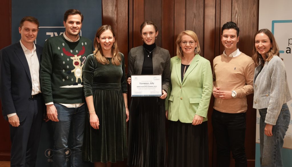 Gruppe von fünf Personen, die in einem rustikalen Raum mit Holzvertäfelung Urkunden halten.