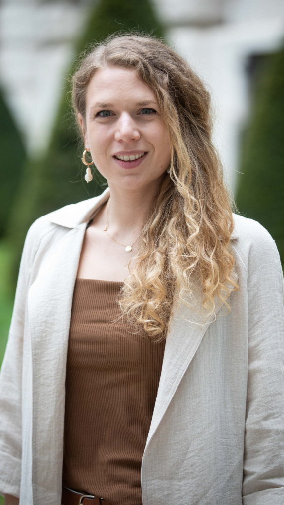 Portrait einer lächelnden Frau mit blonden Haaren im beigen Blazer.