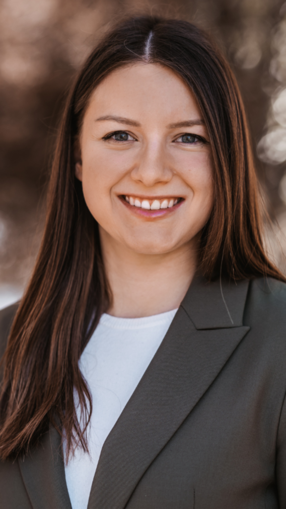 Portrait einer lächelnden Frau mit braunen Haaren im dunklen Blazer.