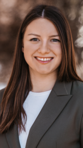 Portrait einer lächelnden Frau mit braunen Haaren im dunklen Blazer.