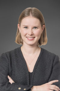 Nahaufnahme einer lächelnden Frau mit blonden Haaren vor grauem Hintergrund.