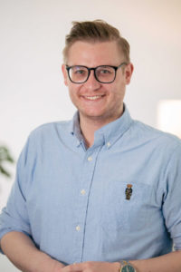Portrait eines Mannes mit Brille im hellblauen Hemd, freundlich lächelnd.