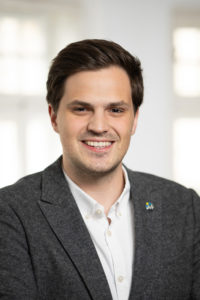 Portrait eines lächelnden Mannes mit dunklen Haaren im grauen Sakko.